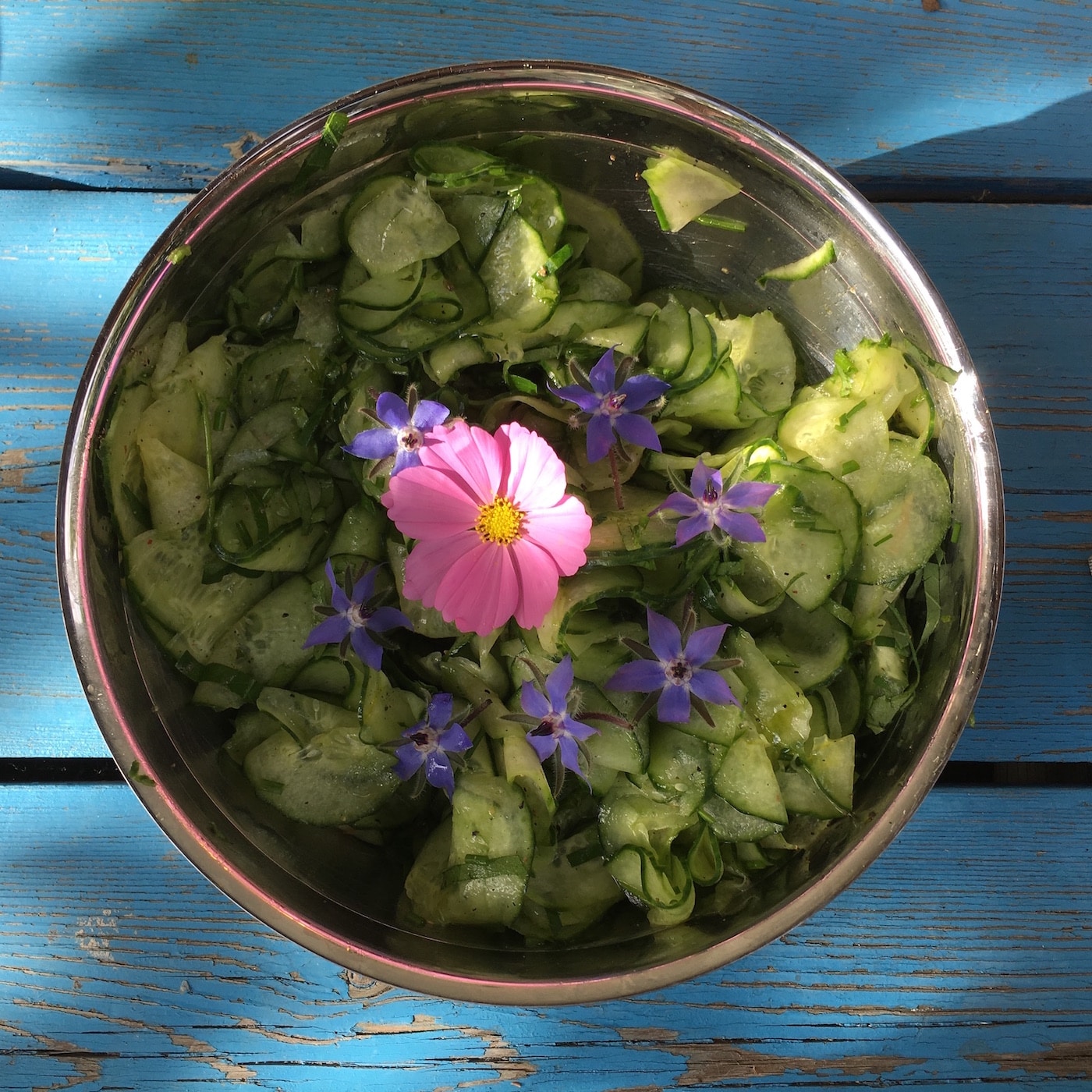 Gurkensalat mit Borretschblüten in einer Metallschüssel auf dem alten blauen Tisch im Erfurter Garten.